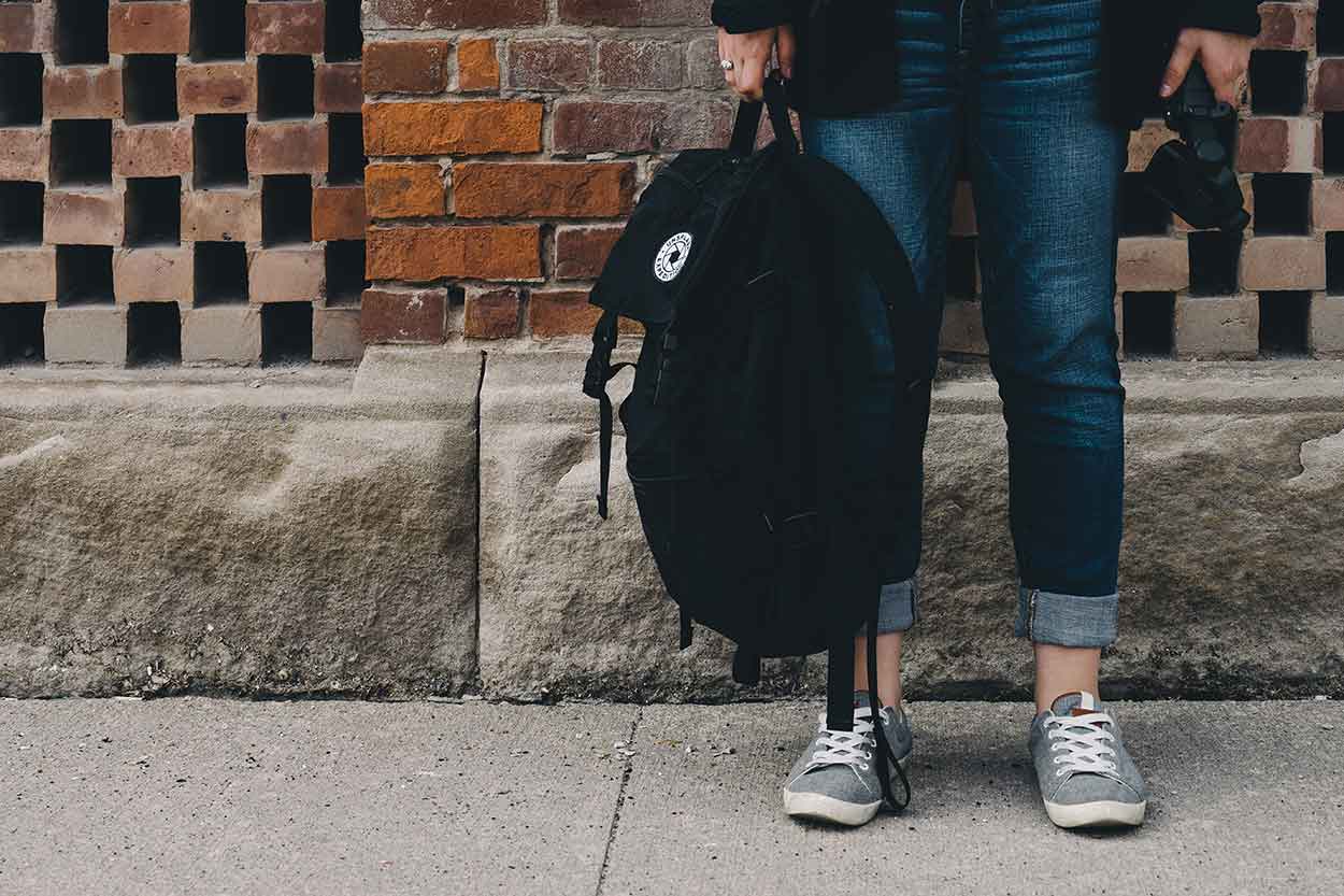 Young person holding bag waiting for parent to arrive in new car