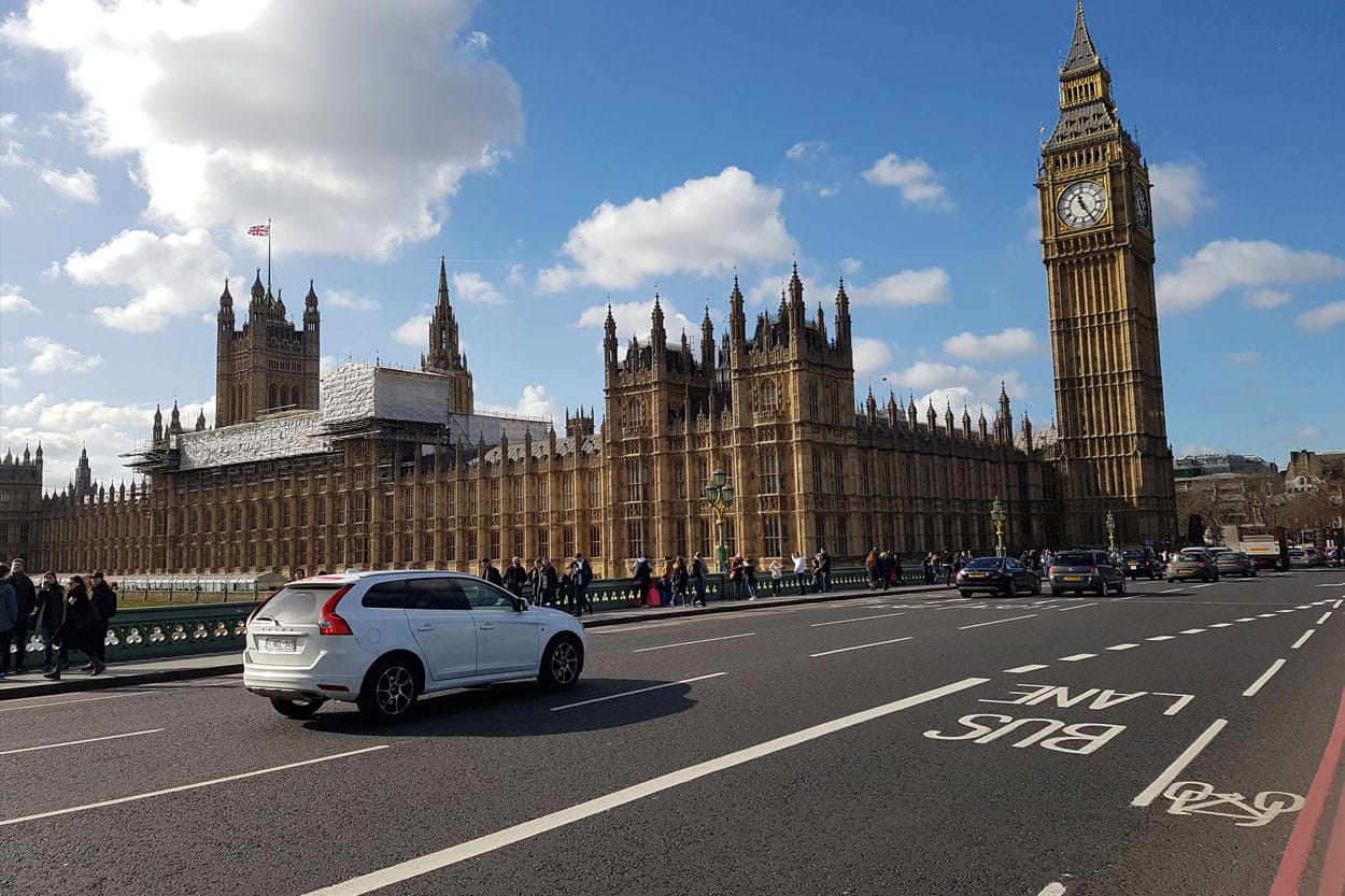 White car bought on finance driving past the houses of parliament in London