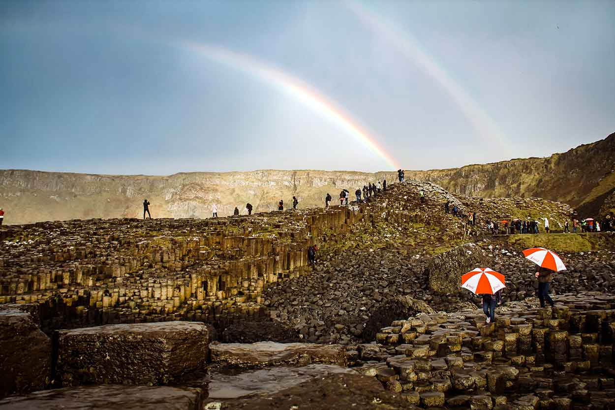 people with umbrellas on giants causeway